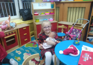 Dziewczynka siedzi z lalką w kąciku zabawek