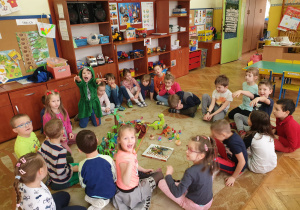 Dzieci siedzą w kole, pośrodku makieta z dinozaurami