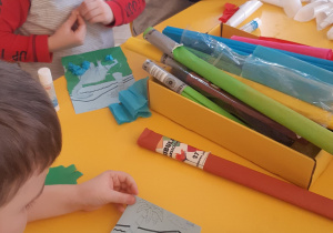 Dzieci wykonują pracę plastyczną- wydzierankę przedstawiającą dinozaura