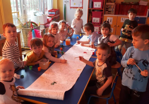 Dzieci malują dinozaury na długiej kartce papieru