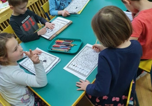 Dzieci kolorują karty pracy przy stolikach