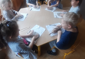 Dzieci siedzące przy stole, tworzą prace plastyczną z gliny