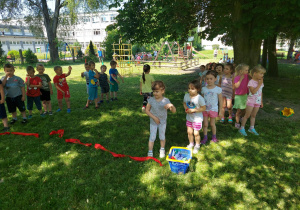 Dzieci ustawione w rzędach, uczestnicza w "konkurencji rzut woreczkiem do kosza"