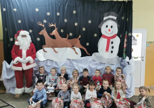 Dzieci z grupy drugiej pozują do zdjęcia z Mikołajem na tle dekoracji świątecznej