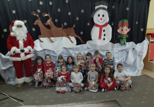 Dzieci z grupy czwartej pozują do zdjęcia z Mikołajem na tle dekoracji świątecznej