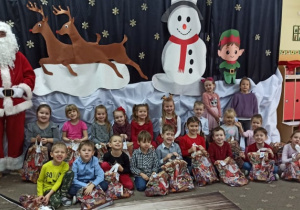 Dzieci z grupy trzeciej pozują do zdjęcia z Mikołajem na tle dekoracji świątecznej