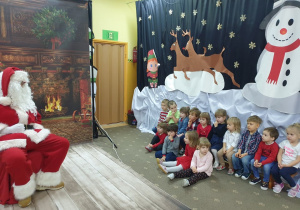 Dzieci siedzące na ławce rozmawiają z Mikołajem