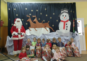 Dzieci pozują do zdjęcia z Mikołajem. W rękach trzymają torby z prezentami.