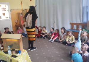 Prowadząca warsztaty, przebrana w strój pszczoły, opowiada dzieciom ciekawostki o pszczołach
