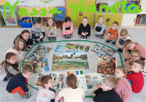Dzieci siedzą naokoło plansz przedstawiających zagadnienia zwiazane z ekologią, przyrodą
