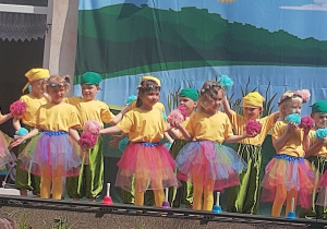 Dzieci ubrane w kolorowe stroje, stoją na tarasie przedszkolnym podczas uroczystości