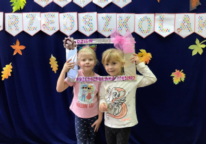 Dziewczynki pozują do zdjęcia na tle napisu Dzień Przedszkolaka,, trzymając ozdobną ramkę