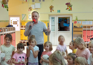 Pan Witek mówiący do widowni przez mikrofon, stoi w otoczeniu przedszkolaków