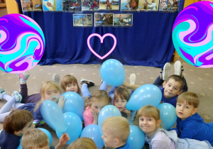 Dzieci leżą na dywanie z niebieskimi balonami, na tle ilustracji przedstawiających prawa dziecka