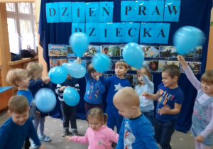 Dzieci bawią się niebieskimi balonami na tle napisu Dzień Praw Dziecka