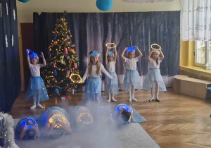Dziewczynki tańczą w strojach świątecznych, trzymając w rękach obręcze