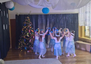 Dziewczynki tańczą w strojach świątecznych, trzymając w rękach obręcze