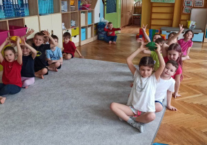 Dzieci uczestniczące w zawodach sportowych, siedzą w dwóch rzędach i podają sobie "jeżyki"