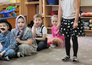 Dziecko przebrane za pieska stoi na "scenie przedszkolnej" obok siedzących dzieci.