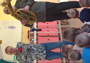 Muzycy prezentują instrument muzyczny róg barytonowy oraz dzwięki, które można zagrać na tym instrumencie