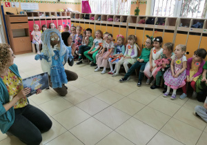 dzieci siedzą w szatni przedszkola i słuchają nauczyciela opowiadającego historię topienia marzanny