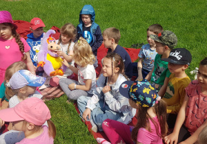 Dzieci siedzą na kocach w ogrodzie przedszkolnym, uczestniczą w warsztatach