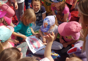 Dzieci uczestniczą w zajęciach warsztatowych o higienie jamy ustnej w ogrodzie przedszkolnym, ogjądają ilustrację przedstawiajacą jamę ustną