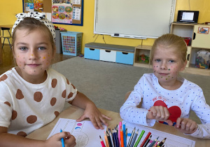 dwie dziewczynki z buzią pomalowana w kropki wykonują przy stole prace plastyczną