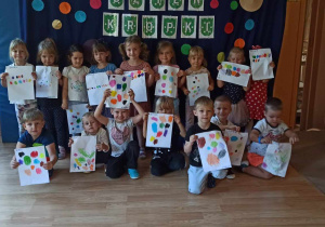 Dzieci pozują do zdjęcia na tle dekoracji przedstawiającej różnokolorowe kropki