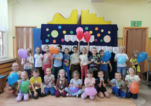 Dzieci pozują do zdjęcia z balonami na tle dekoracji w Dniu Przedszkolaka
