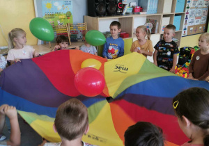 Dzieci podrzucają balony, stojąc naokoło chusty animacyjnej