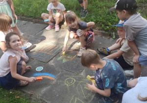 Dzieci rysują kredą na chodniku w ogrodzie przedszkolnym