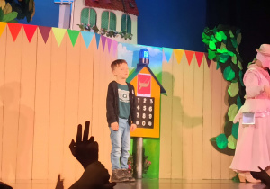 Chłopiec na scenie teatru na tle dekoracji lasu, domu