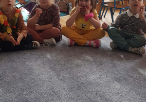 Dzieci przebrane w stroje jesienne siedzą na dywanie.Przed nimi talerz z suszonymi owocami