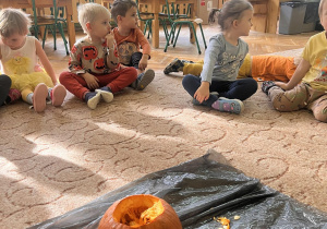 Dzieci przebrane w stroje w kolorze pomarańczowym oglądają dynię, jej pestki