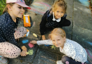 dziewczynki malują kolorową kredą po chodniku
