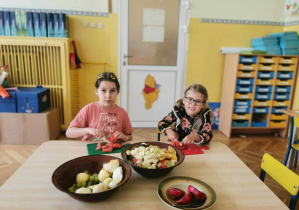 Dziewczynki kroją owoce na deseczkach do sałatki