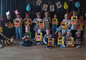 Dzieci przebrane w stroje kotów pozują do zdjęcia na tle dekoracji z napisem "dzień kota", trzymają w ręku prace plastyczną przedstawiającą kota