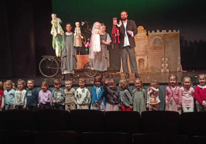 Dzieci pozują do zdjęcia pod sceną teatru, na której stoją aktorzy