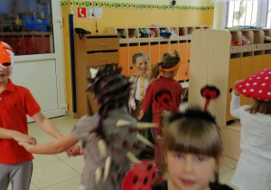 Dzieci z grupy ,,Leśne duszki’ tańczą w szatni przedszkolnej na balu jesieni. Dziewczynki poprzebierane są w stroje lisków, wiewiórek, grzybków. Dzieci sa uśmiechnięte i rozbawione. W tle widoczne są szafki z ubraniami dzieci.