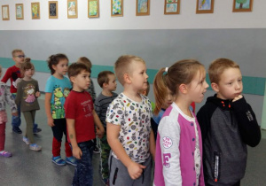 Przedszkolaki z grupy „Leśnych duszków” stoją parami na korytarzu szkoły. Dzieci z zaciekawieniem słuchają objasnień osoby, która opowiada im o szkole.