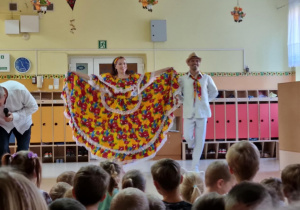 Tancerze w barwnych strojach na scenie przedszkola, prezentują układ tańca