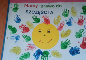 Praca plastyczna przedstawiająca słońce, odciśnięte dłonie dzieci oraz napis