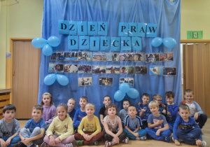 Dzieci pozują do grupowego zdjęcia na tle dekoracji przedstawiającej napis oraz obrazki o tematyce praw dziecka