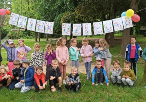 pDzieci pozują do zdjęcia grupowego na tle napisu "Dzień Dziecka"