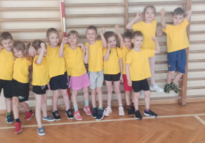 Dzieci ubrane w stroje sportowe, pozują do zdjęcia na tle drabinek na sali sportowej