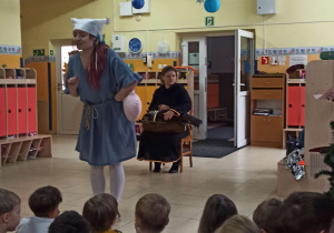 Prowadząca audycję stoi przed dziećmi, opowiadając im o lirze