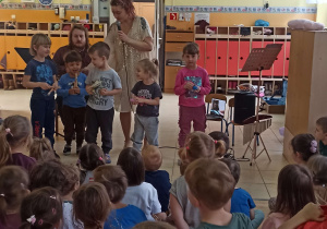 Dzieci stoją na scenie przy muzykach