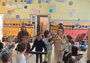 Dzieci stoją na scenie obsrwując artystkę, grającą na saksofonie