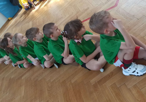 Dzieci siedzące w rzędzie, oczekujące na kolejną konkurencję sportową